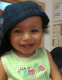 smiling baby wearing a cap and a blouse with the words I Like To Smile