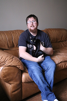 a young man sits on a sofa holding a black cat in his arms