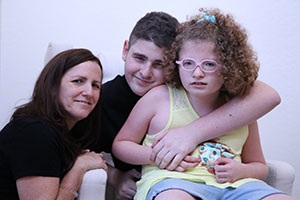woman, teenage boy, and little girl smiling for camera; the boy has his arm around the little girl