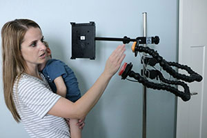 A young woman, holding toddler son, taps a switch that is mounted to a pole