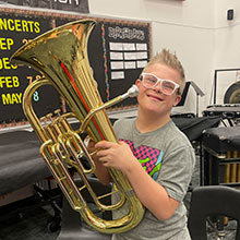 teenage boy holds up a brass tuba-shaped instrument