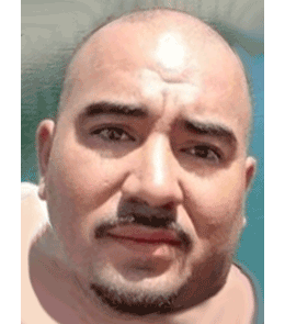 Hispanic male with brown eyes and bald head with mustache and beard.