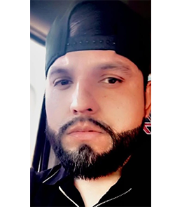 Male with a full beard wearing a backwards baseball cap