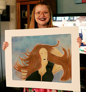 17-year-old girl holds up a sample of her artwork.