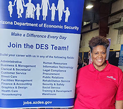 woman standing next to a sign that reads "Join the DES Team!"