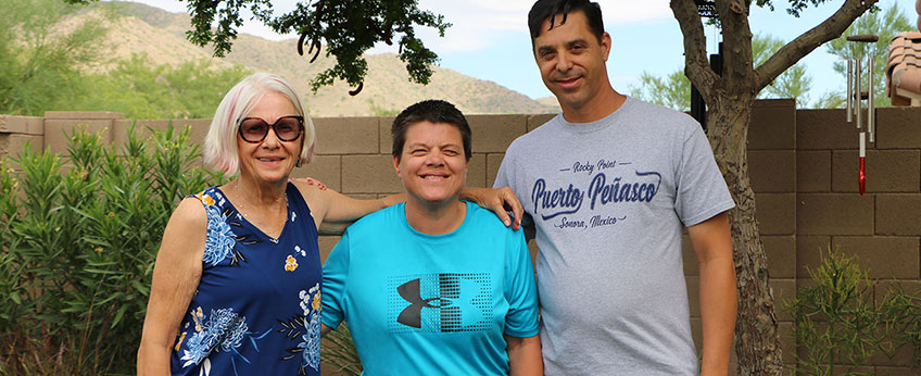 two women and a man stand together in a backyard