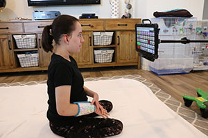 Teenage girl, sitting on the floor, stares at an electronic table that is mounted to a pole.