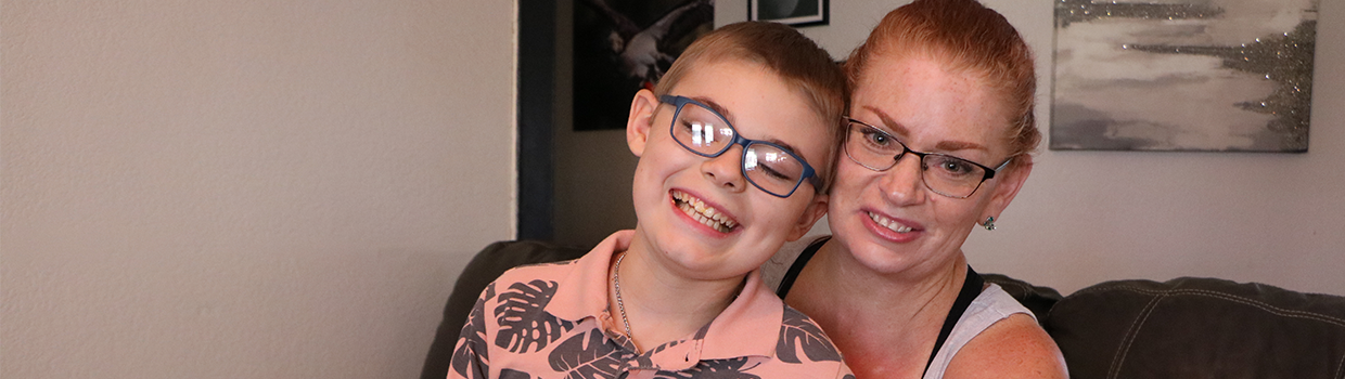 A smiling 12-year-old boy sits on his mother’s lap for a quick photo.