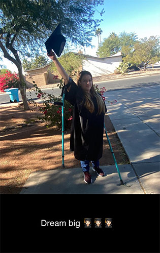 Young woman dressed in a graduation gown and raises her cap in celebration