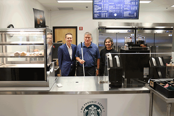 two men and a woman stand behind a counter with the Starbuck's logo on the front