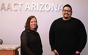 a woman and a man stand before a sign that reads "AACT Arizona"