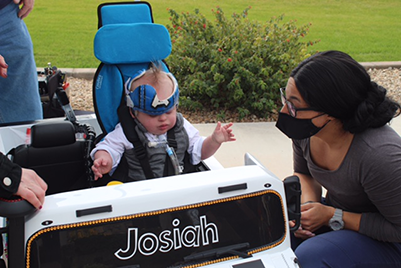toddler boy in toy car; woman kneeling next to it