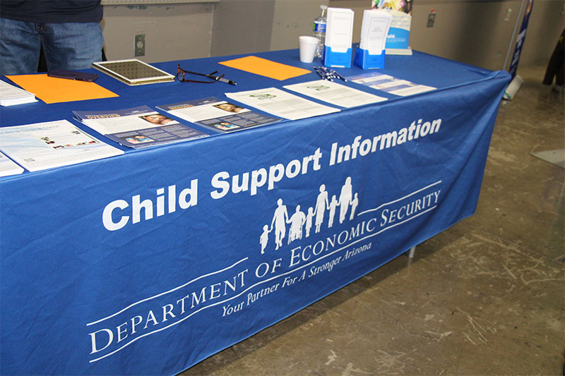 a table is draped in a tablecloth with the words "Child Support Information"; there are piles of flyers and pamphlets on the table top