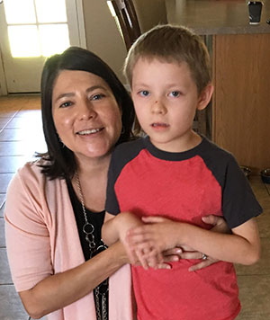 Mom crouching down with her arms around her six-year old son.