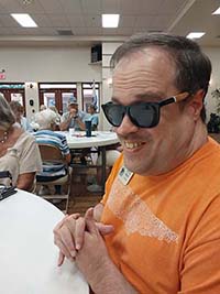 Man wearing a T-shirt and sunglasses smiles while sitting at a table