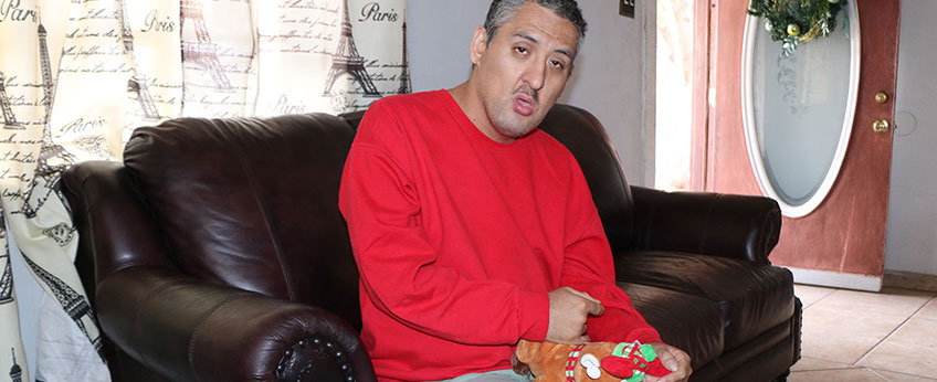 Man sitting on couch holding stuffed reindeer toy.