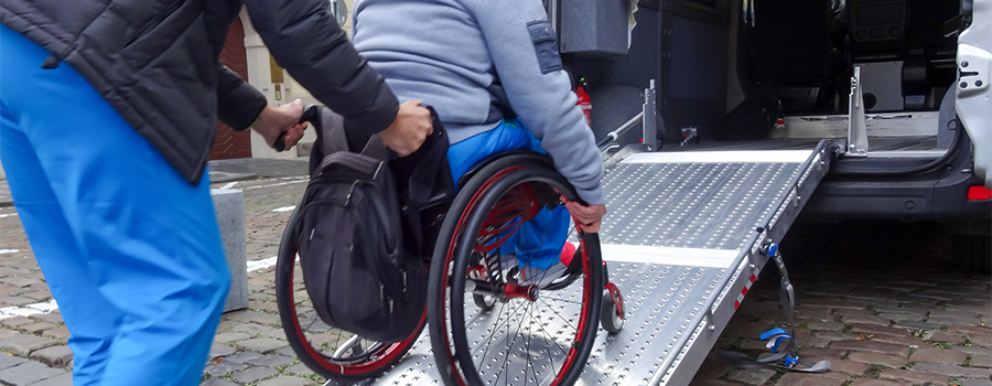 Individual pushing a person who is in a wheelchair up a ramp.