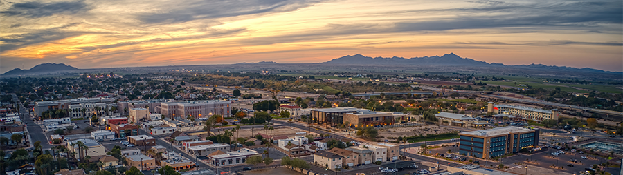 Aerial view of a cityscape at sunset with mountains in the background and colorful sky.
