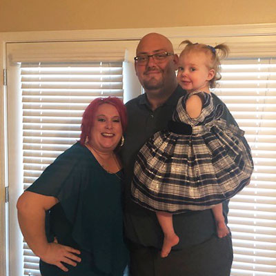 A woman stands next to her husband who is holding their daughter