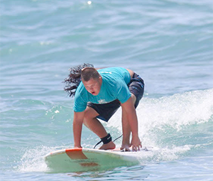 A surfer in a teal T-shirt balancing low on a surfboard in a blue ocean.