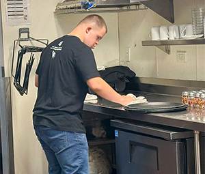 Person cleaning a counter in a commercial kitchen setting.