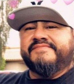 A Hispanic man with brown eyes and a black beard is wearing a white baseball cap