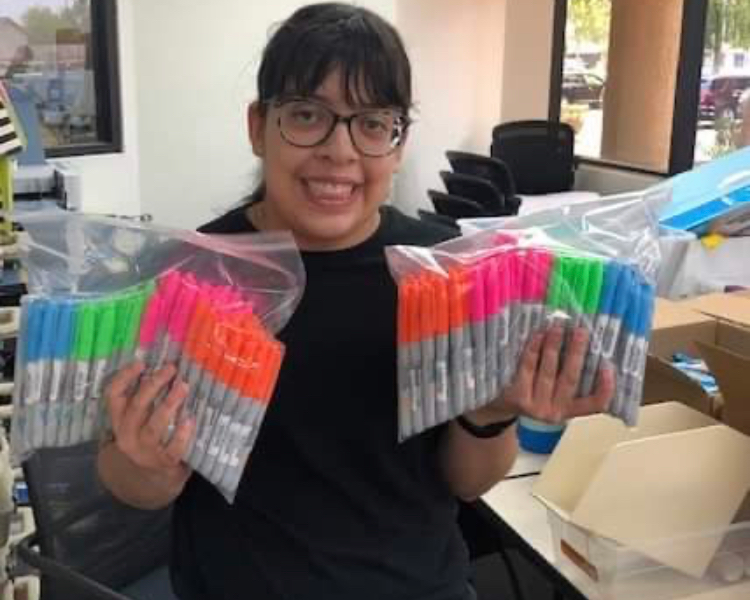 a young girl smiles while holding plastic bags filled with colorful markers