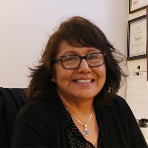 A dark-haired woman dressed in black and wearing glasses smiles cheerfully