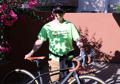 Man wearing sunglasses and a ball cap stands with his bicycle out on his enclosed patio