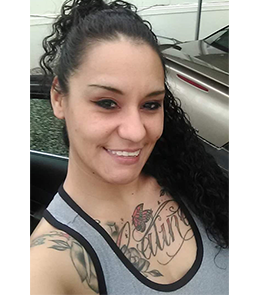 A Hispanic female with brown eyes, black hair and large tattoo across chest.