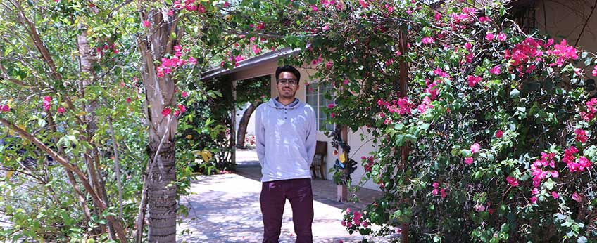 young man standing in front of an arch of bougainvillea