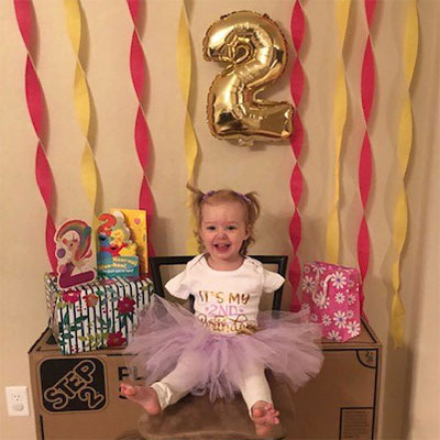 A toddler in a pink tutu sits surrounded by birthday cards, signs, a balloon and streamers