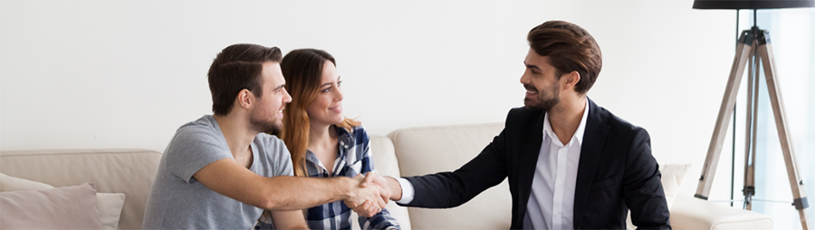 Two men shaking hands on a sofa while a woman looks on.
