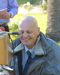picture of smiling man in a wheelchair in front of a microphone at a podium