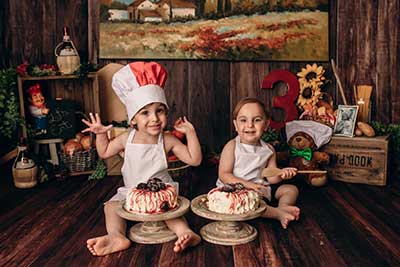 Two 3-year-old brothers, each with a cake in front of them, celebrate their birthday.