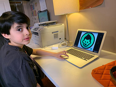 a young boy looks towards the camera while using his laptop