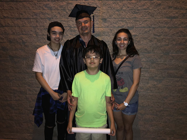 man in graduation cap and gown surrounding by three children