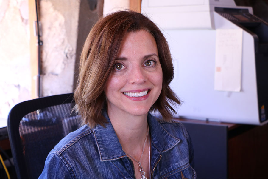 Head shot of a young woman with short brown hair wearing a denim jacket looks straight at the camera and smiles.