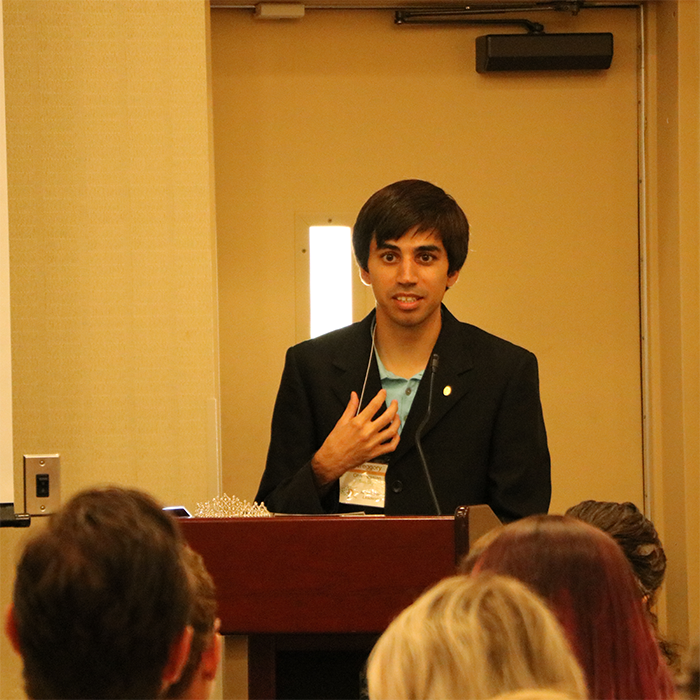 a young man stands behind a podium speaking before an audience