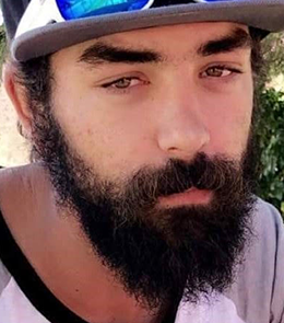 A White male with brown eyes, brown hair, mustache and beard.