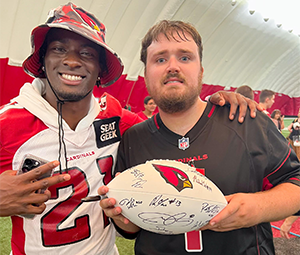 Two people in football jerseys inside a dome, one holding an autographed football.