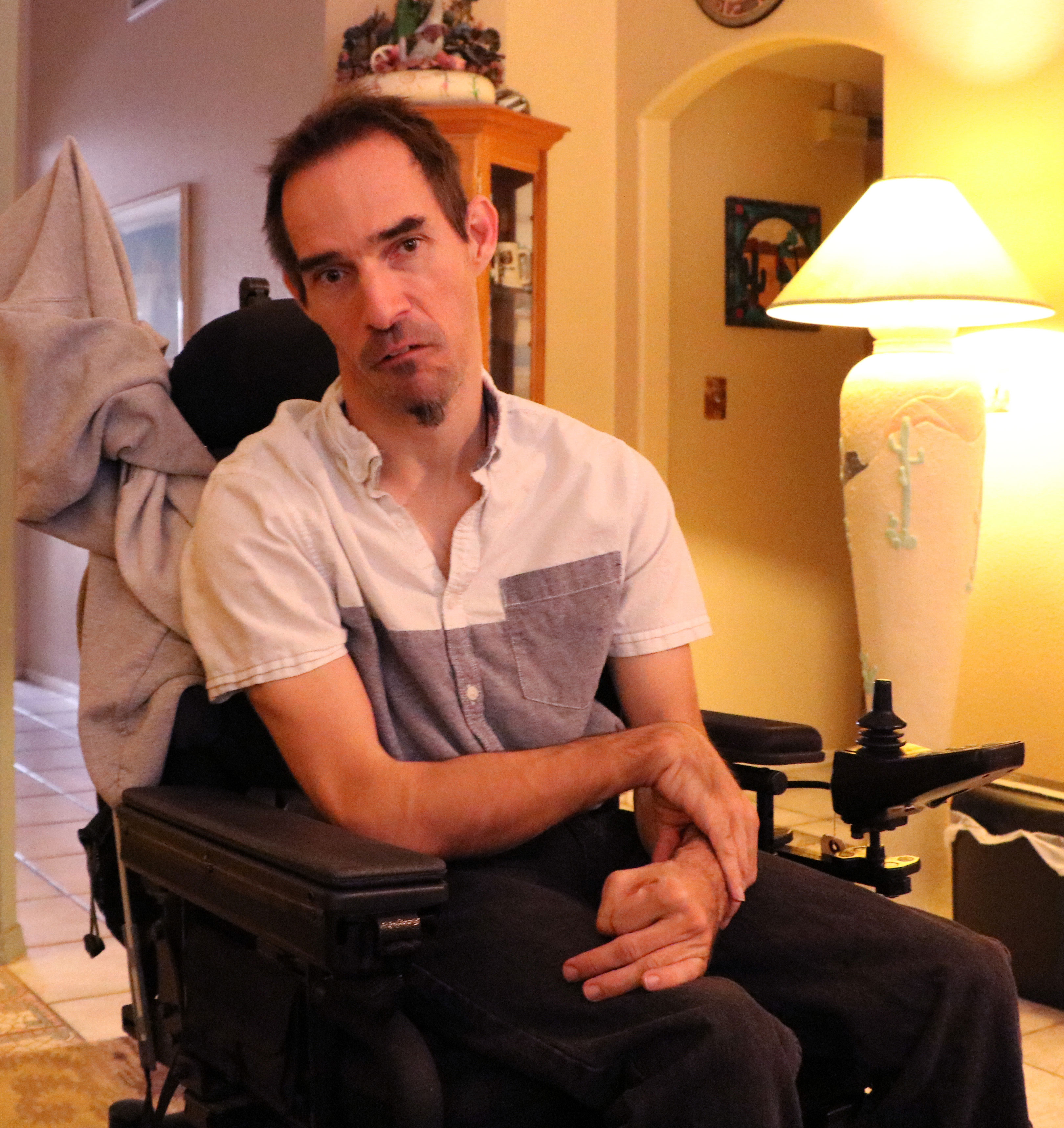 Man with a serious look on his face, sits in a power wheel chair at his home in Mesa
