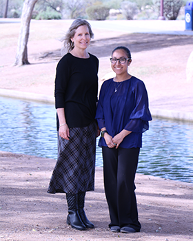 Tall woman wearing a skirt stands with her colleague in front of a water canal in a city park