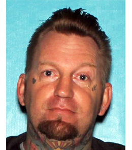 A white male with blue eyes, blonde hair, goatee, tattoos under each eye and on throat