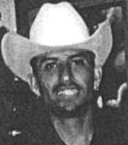 A Hispanic man with brown eyes, brown hair, and a goatee is wearing cowboy hat and a black t-shirt.