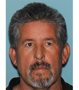 Hispanic man with brown eyes, short, graying, brown hair, and a goatee wearing a black collared shirt