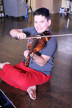 a boys sits cross-legged on the floor, playing a violin