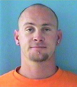 A white man with a shaved head, blue eyes, a chin piercing, and a goatee is wearing an orange t-shirt.