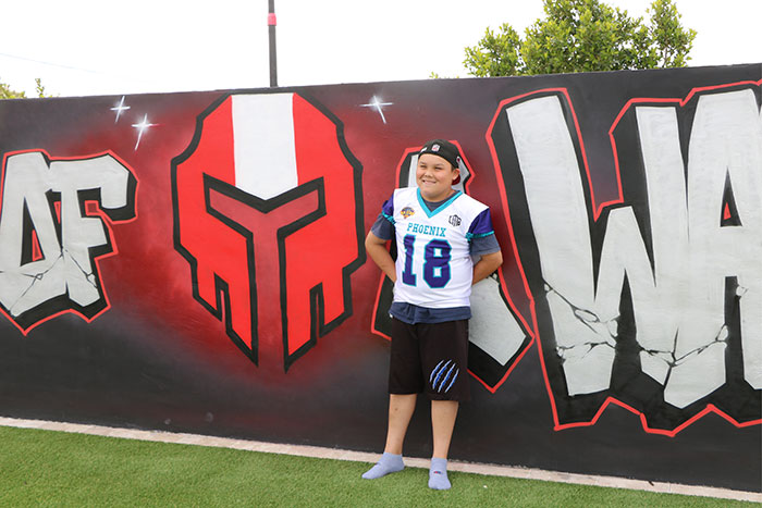 Boy wearing his team’s jersey stands in front of a painted wall.
