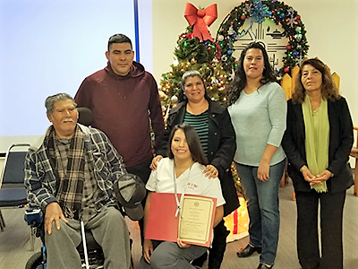 a young woman holds a certificate; other family members stand in the background